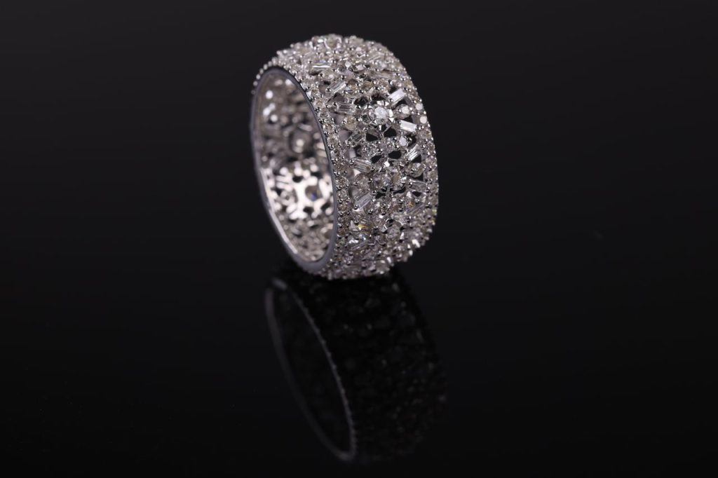 Close-up of an ornate silver ring with intricate detailing, set on a reflective black background.